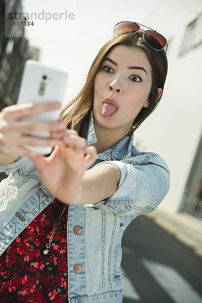 Grimassierende junge Frau  die mit einem Selfie nach draußen geht.