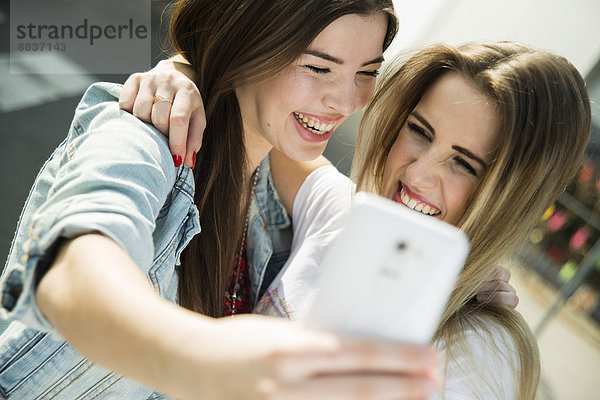 Zwei glückliche junge Frauen  die mit einem Selfie nach draußen gehen.