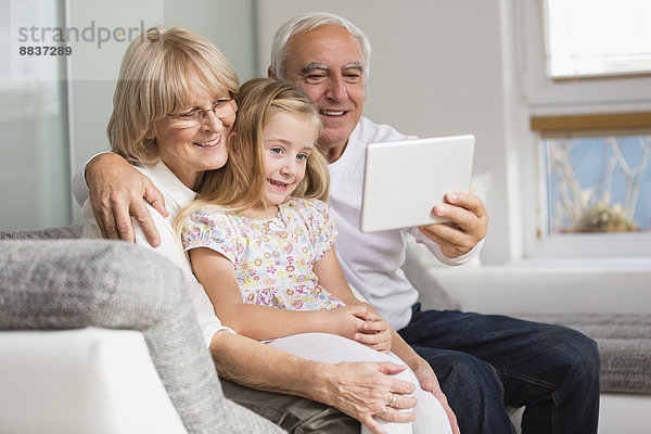 Seniorenpaar und Enkelin beim Betrachten des digitalen Tabletts zu Hause