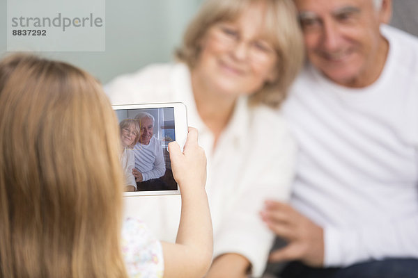 Kleines Mädchen fotografiert ihre Großeltern mit digitalem Tablett zu Hause.