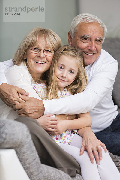 Porträt eines älteren Paares mit Enkelin auf Sofa im Wohnzimmer