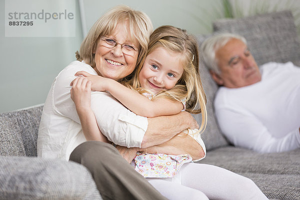 Porträt einer älteren Frau  die ihre Enkelin auf dem Sofa im Wohnzimmer umarmt.