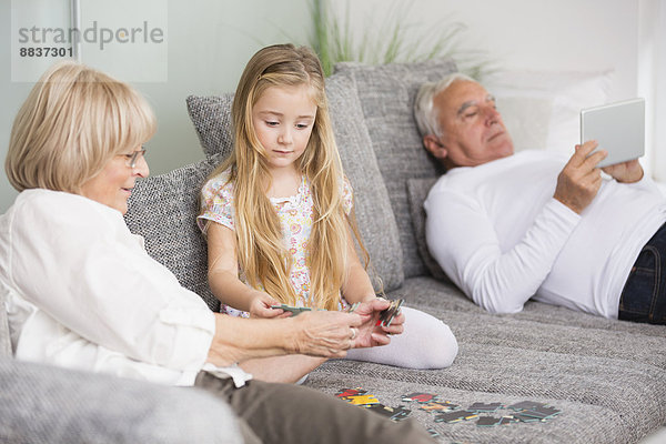 Seniorin und Enkelin beim gemeinsamen Spielen auf dem Sofa im Wohnzimmer