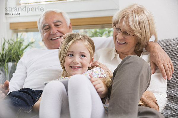 Seniorenpaar und Enkelin sitzend mit digitalem Tablett auf Sofa im Wohnzimmer