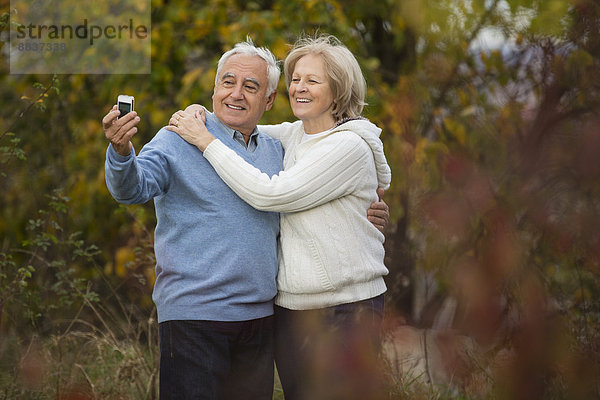 Porträt eines lächelnden Seniorenpaares beim Selbstporträt mit Smartphone