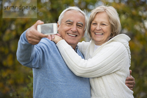 Porträt eines lächelnden Seniorenpaares beim Selbstporträt mit Smartphone