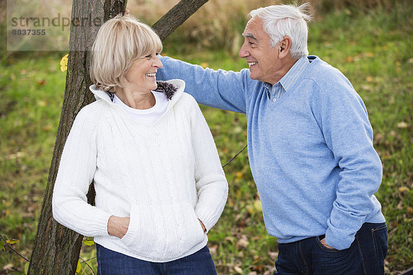 Lächelndes älteres Paar  das sich an den Baumstamm lehnt