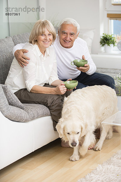 Seniorenpaar sitzt nebeneinander auf Sofa im Wohnzimmer  Hund im Vordergrund