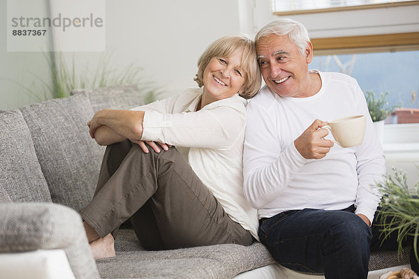 Lächelndes Seniorenpaar Seite an Seite auf dem Sofa im Wohnzimmer