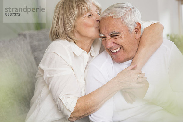 Seniorin beim Küssen ihres Mannes im Wohnzimmer