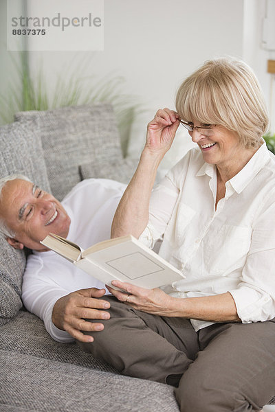 Lächelndes Seniorenpaar mit Buch auf Sofa im Wohnzimmer