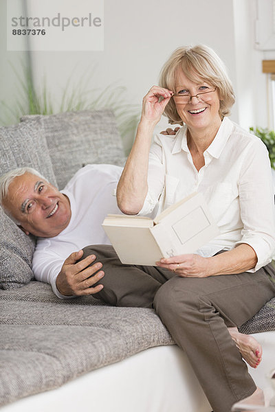 Seniorenpaar mit Buch auf Sofa im Wohnzimmer