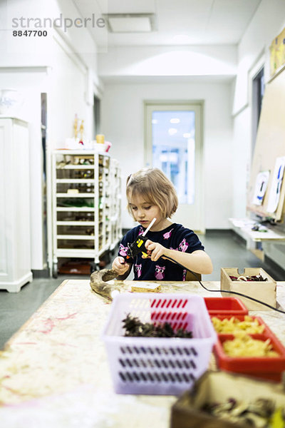 Mädchen mit Klebepistole am Tablett im Kindergarten-Kunstunterricht