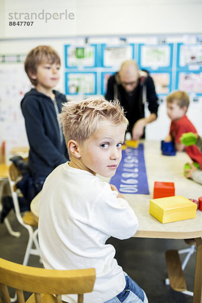 Porträt des selbstbewussten Kindergartenjungen in der Kunstklasse mit Lehrerin und Freunden