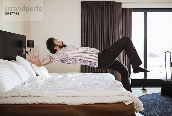 Volle Länge des Geschäftsmannes beim Springen auf dem Bett im Hotelzimmer