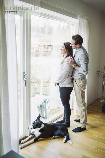 Seitenansicht des Paares beim Blick durchs Fenster zu Hause