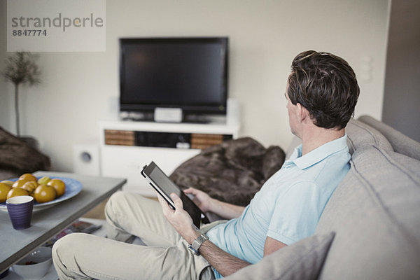 Seitenansicht des Mannes mit digitalem Tablett auf dem Sofa zuhause