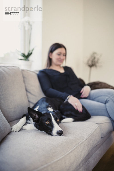 Frau sitzend mit Hund auf Sofa zu Hause