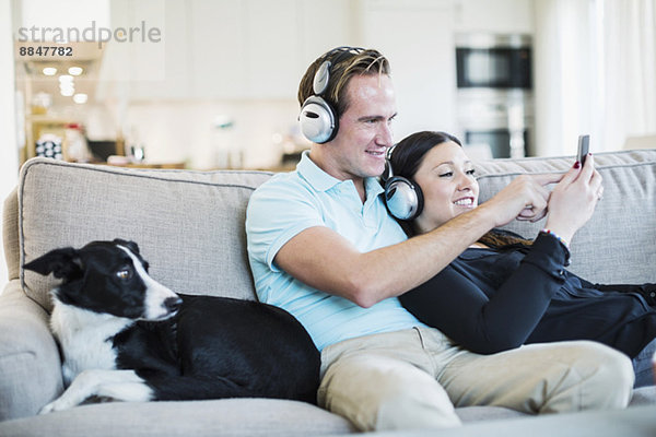 Paar hört Kopfhörer mit Hund auf Sofa