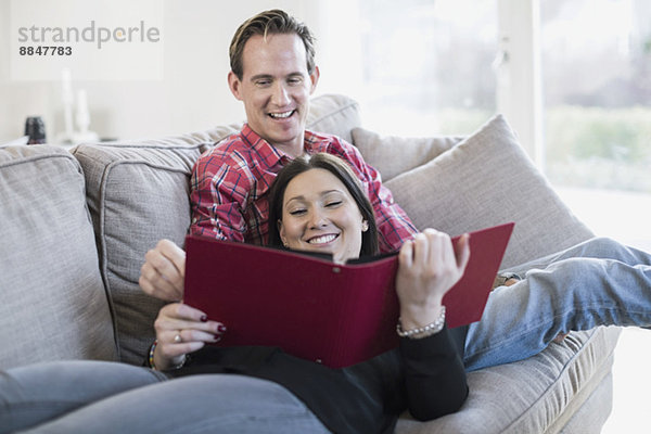 Glückliches Paar beim gemeinsamen Betrachten des Fotoalbums auf dem Sofa