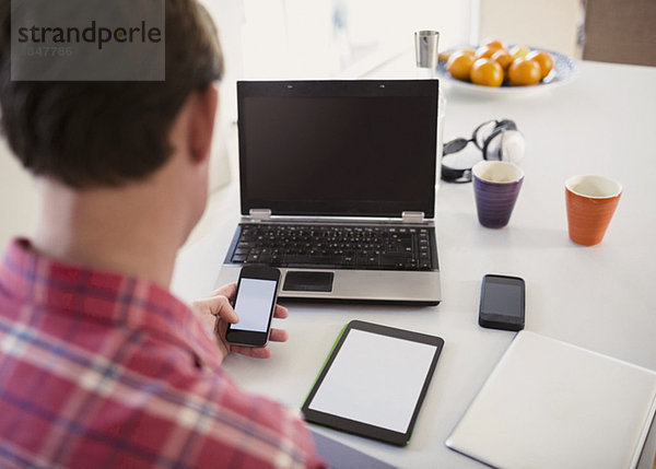 High-Winkel-Ansicht des Menschen mit Smartphone mit digitalem Tablett und Laptop auf dem Tisch