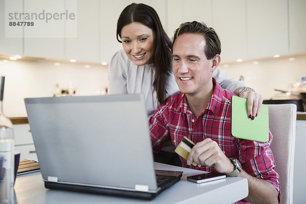 Lächelndes Paar online einkaufen durch Kreditkarte und Laptop zu Hause