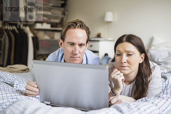 Paar mit Laptop im Bett zu Hause liegend