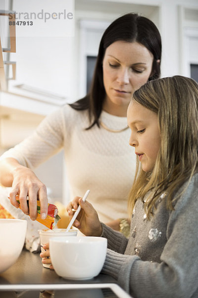 Mutter und Tochter fügen Geschmack in Tasse in der Küche hinzu