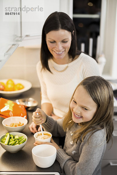 Glückliche Mutter und Tochter bei der Zubereitung von Salat in der Küche