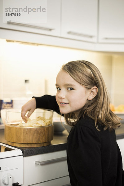 Seitenansicht Porträt eines Mädchens  das Kartoffelchips an der Küchentheke isst.