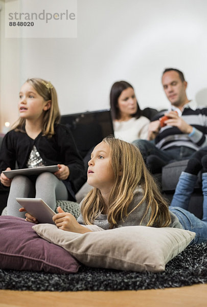 Schwestern mit digitalen Tabletten und Eltern im Hintergrund zu Hause