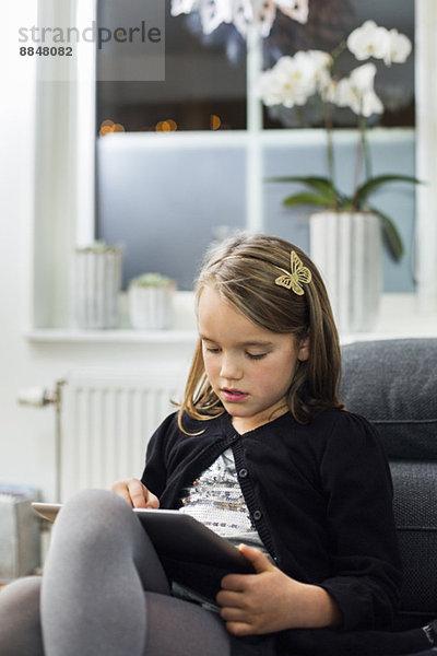 Mädchen mit digitalem Tablett auf Sofa im Wohnzimmer