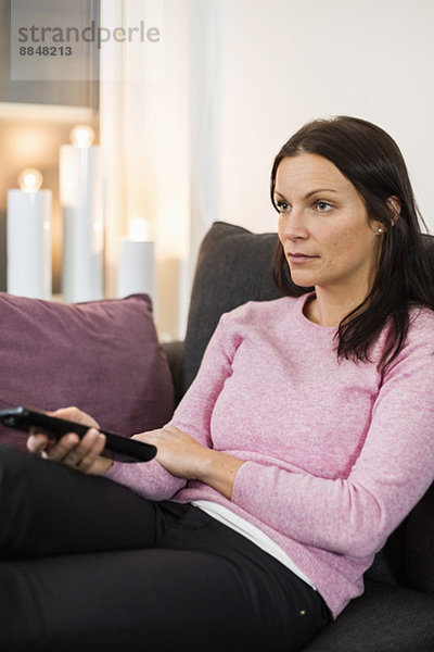 Mittlere erwachsene Frau  die zu Hause auf dem Sofa fernsieht.