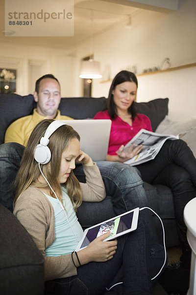 Mädchen hört Musik auf digitalem Tablett mit Eltern im Hintergrund zu Hause