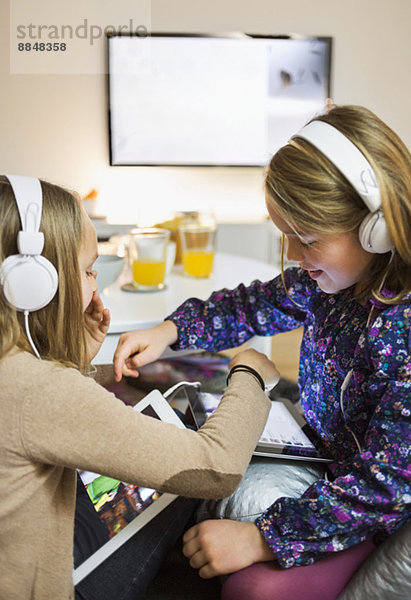 Schwestern beim Musikhören auf digitalen Tabletts im Wohnzimmer