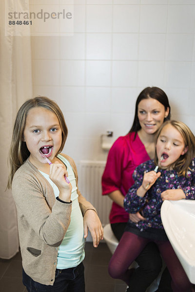 Porträt eines Mädchens beim Zähneputzen mit Mutter und Tochter im Bad