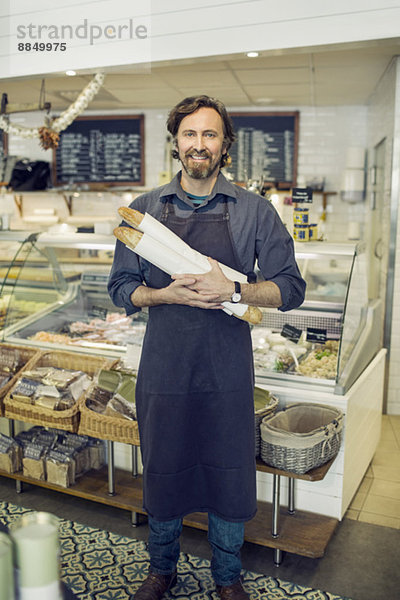 Porträt eines reifen Bäckers mit Brotlaiben im Supermarkt