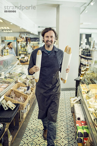 Porträt eines reifen Bäckers mit Brotlaiben im Supermarkt