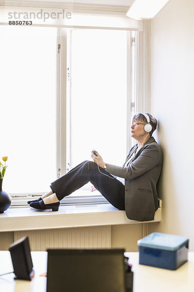 Volle Länge der Geschäftsfrau beim Musikhören auf der Fensterbank