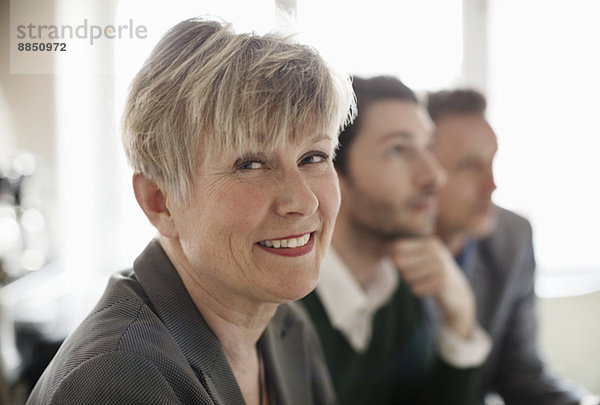 Porträt einer glücklichen Geschäftsfrau mit Kollegen im Hintergrund im Büro