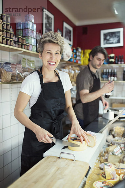 Porträt der glücklichen Verkäuferin beim Käseschneiden an der Theke im Supermarkt