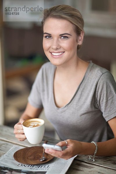 Porträt einer jungen Frau im Café mit Kaffeetasse und Handy