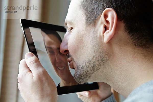 Mittlerer Erwachsener Mann  der den Bildschirm eines digitalen Tabletts küsst