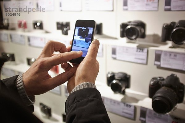 Mittlerer Erwachsener Mann fotografiert Kameras im Laden mit Smartphone