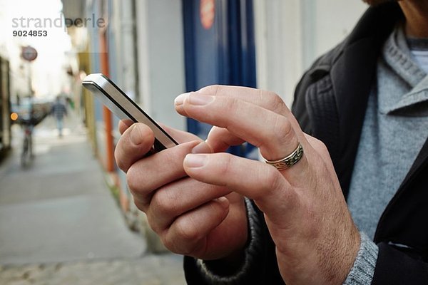 Mittlerer Erwachsener Mann auf dem Bürgersteig mit Touchscreen auf dem Smartphone