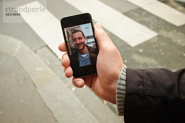 Mid Erwachsene Mann auf dem Bürgersteig halten Smartphone mit Foto auf dem Bildschirm