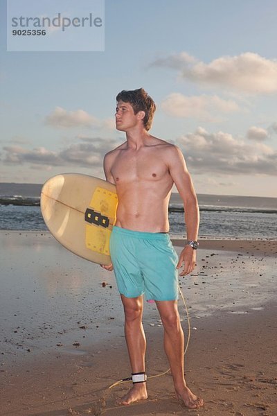 Surfer mit Surfbrett am Strand stehend