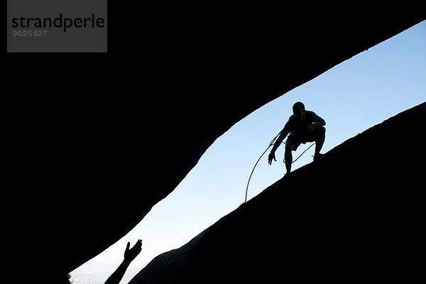 Silhouette junger  männlicher Kletterer  die auf dem Felsen aufeinander zugehen.