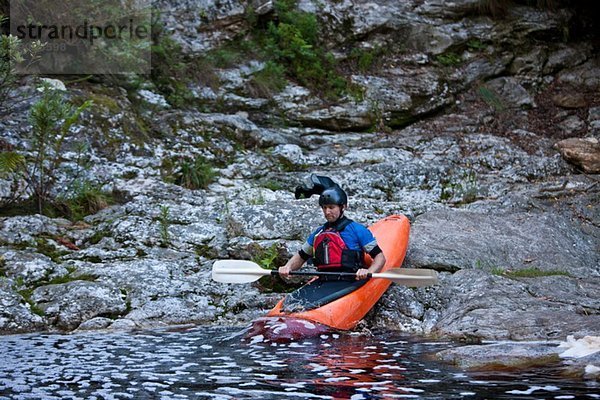 Mittlerer Erwachsener Mann  der Kajak vom Wasserrand in den Fluss bewegt.