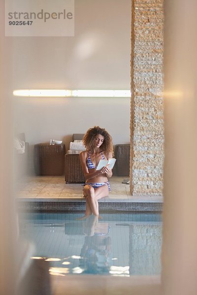 Einsame junge Frau liest Buch am Rande des Schwimmbades